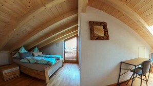 Een zolderkamer met een hoogslaper, een bureau en een stoel.