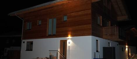 Una casa de madera de dos pisos con fachada blanca, una escalera y un pequeño porche.