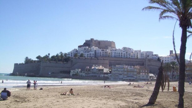Une plage avec un fort historique qui domine l’océan, une étendue de sable et des palmiers.