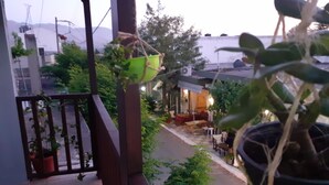 A balcony with potted plants, a view of a street, and a building with outdoor seating. - Hospitality Home in Asimi , with great location (HERAKLEION,GRETE)