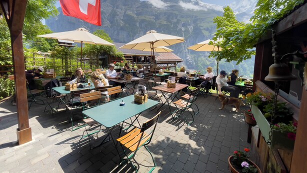 An outdoor café with tables and chairs, a Swiss flag, and a mountain view. - Pension Gimmelwald (Gimmelwald)