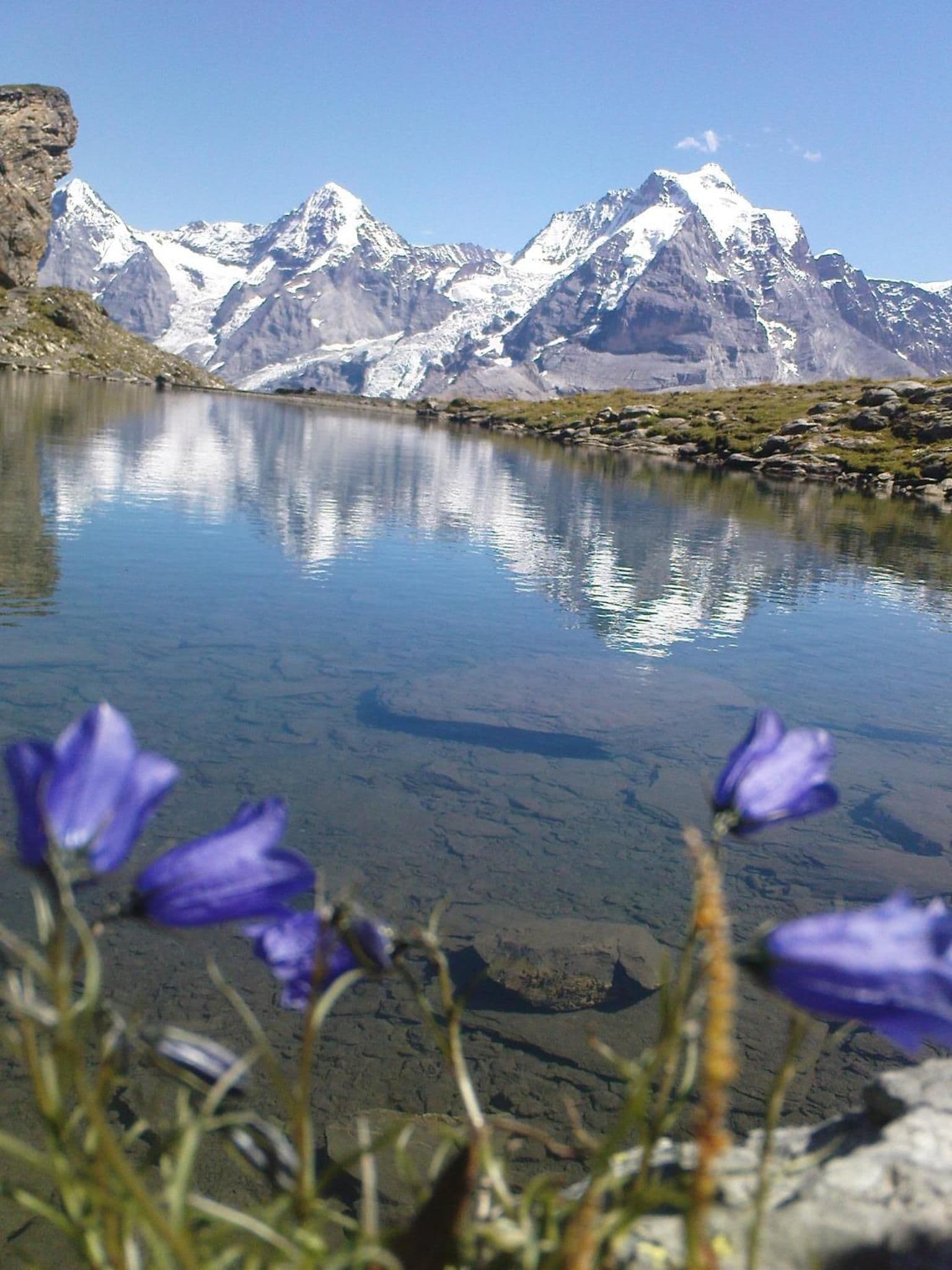 Ein Bergsee mit klaren Spiegelungen, umgeben von schneebedeckten Gipfeln.