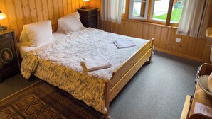 A wooden-paneled room with a bed, a nightstand, a lamp, and a window with curtains. - Pension Gimmelwald (Gimmelwald)