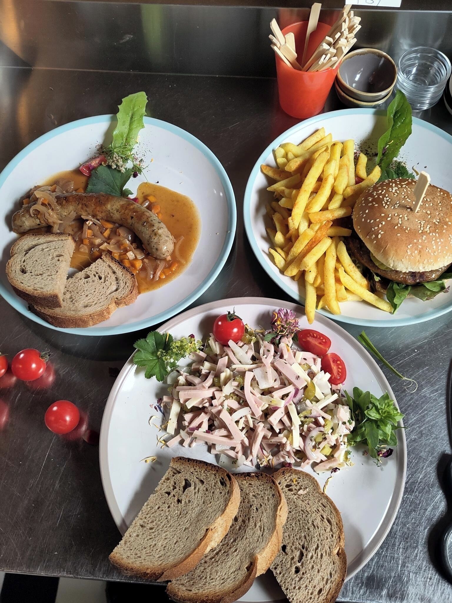 Three plates of food on a stainless steel table.