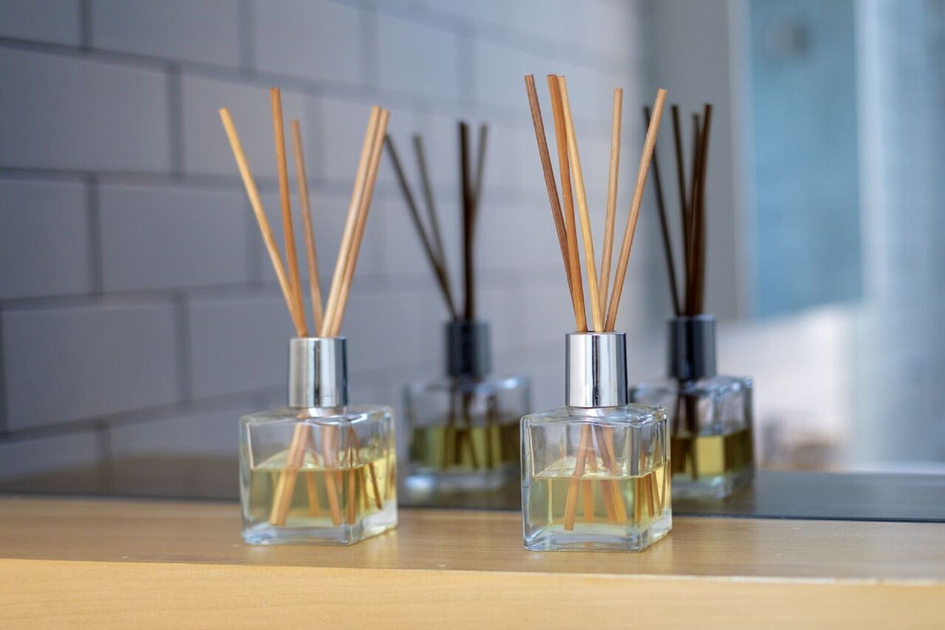 Trois bouteilles en verre contenant des diffuseurs à bâtonnets, posées sur une surface en bois.