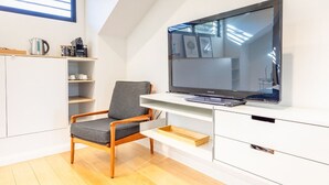 Ein modernes Wohnzimmer mit Flachbildfernseher, Holzstuhl, weißen Schränken und Holzboden.