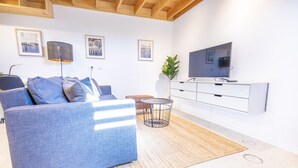 Ein modernes Wohnzimmer mit einem blauen Sofa, einem Fernseher, einem kleinen Beistelltisch und einer Pflanze.