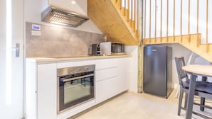 Eine kompakte Küche mit Einbauofen, Mikrowelle und Kühlschrank. Eine Holztreppe führt zu einer oberen Ebene.