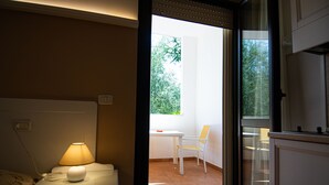 Une chambre à coucher avec une table de chevet, une lampe et une fenêtre donnant sur un balcon équipé d’une chaise et d’une table.
