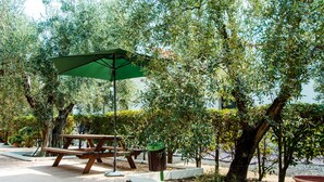 Un espace extérieur aménagé avec une table et un banc en bois, un parasol vert et une poubelle.