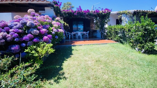 A patio area with a table and chairs, surrounded by lush purple flowers and greenery. - Appartamento Cala D'Ambra (San Teodoro)