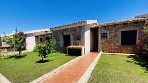 A row of stone buildings with tiled roofs, a paved walkway, and small trees. - Appartamento Cala D'Ambra (San Teodoro)