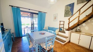 A dining area with a checkered tablecloth, blue chairs, a blue sofa, and a staircase leading to an upper level. - Appartamento Cala D'Ambra (San Teodoro)