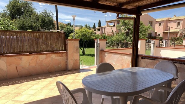 An outdoor patio area with a round table and four chairs, surrounded by stone walls and a wooden pergola. - I Geranei 3 San Teodoro Centro (San Teodoro)