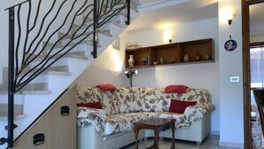 A living room with a sofa, a small table, a staircase, and wall-mounted shelves. - I Geranei 3 San Teodoro Centro (San Teodoro)
