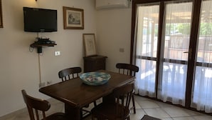 A dining area with a wooden table, chairs, a blue bowl, a television, framed pictures, and an air conditioning unit. - I Geranei 3 San Teodoro Centro (San Teodoro)