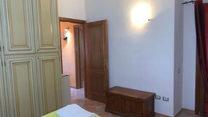 A room with a bed, a wooden bench, a door, and a wall-mounted light fixture. - Appartamento Max con Giardino (Agrustos)