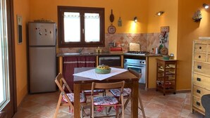 A compact kitchen with a refrigerator, stove, and dining table with chairs. - Appartamento Max con Giardino (Agrustos)