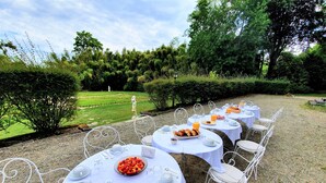 Ein Essbereich im Freien mit runden Tischen, gedeckt für eine Mahlzeit, umgeben von Grünpflanzen und Blick auf einen Garten.