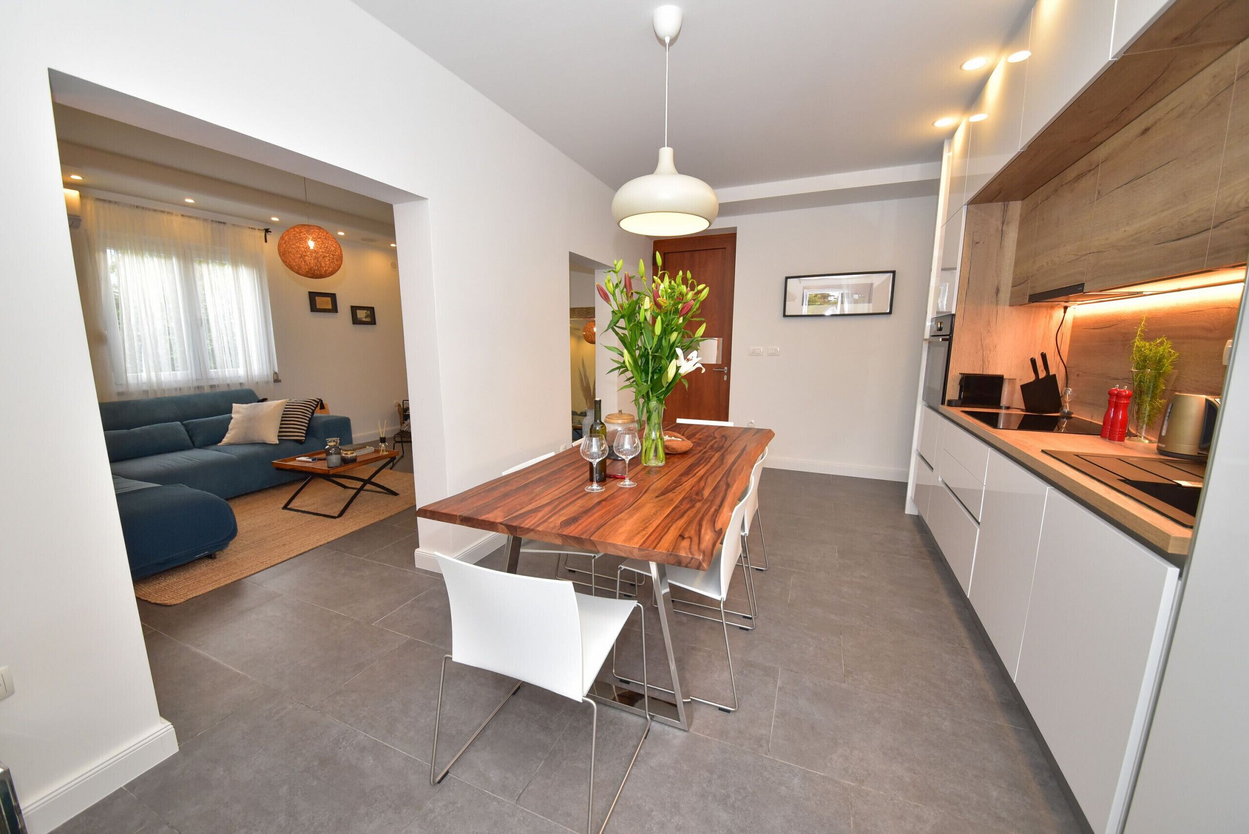 A modern kitchen with white cabinets, a wooden countertop, and a hanging pendant light.