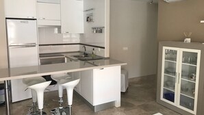 Una cocina moderna con armarios blancos, un lavamanos integrado y una zona de bar con dos taburetes.