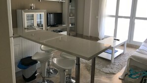 Una cocina compacta con una isla central, taburetes de bar, televisor integrado y un comedor con mesa y sillas.
