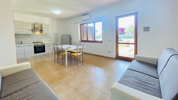 A modern kitchen with white cabinets, a dining table with chairs, and a grey sofa. - Residence La Cinta 5 (San Teodoro)