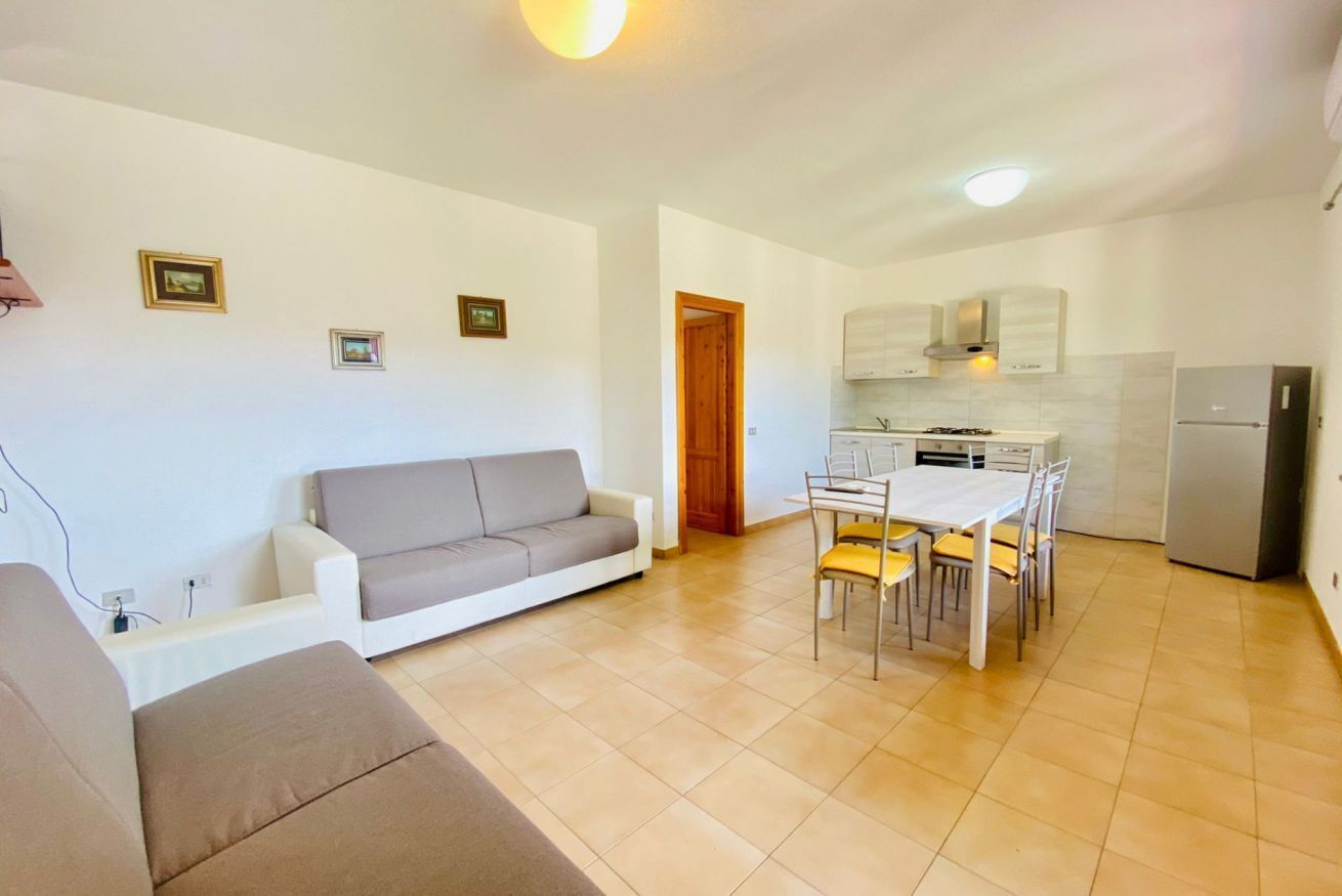 A compact living space with a sofa, dining table, chairs, a kitchenette, and a refrigerator.