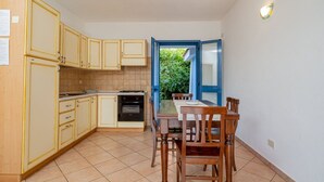 Une cuisine compacte avec des meubles en bois, une table à manger avec des chaises, et une vue sur la verdure par une porte ouverte.