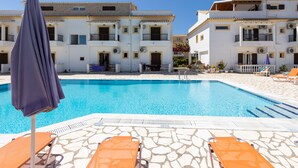 A swimming pool with lounge chairs and umbrellas, surrounded by white buildings with balconies. - Dora Pool Studios by Konnect, 150m from the Beach (Corfu)