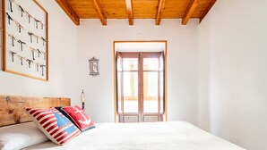 Un dormitorio con techo de madera, una cama con ropa de cama blanca y una ventana con contraventanas de madera.