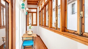 Un estrecho pasillo con vigas de madera y ventanas amplias, una mesa con sillas y un jarrón con flores.