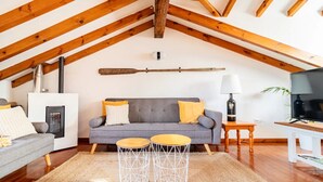 Una sala de estar acogedora con un sofá gris, dos mesas redondas de madera, una chimenea y un televisor.