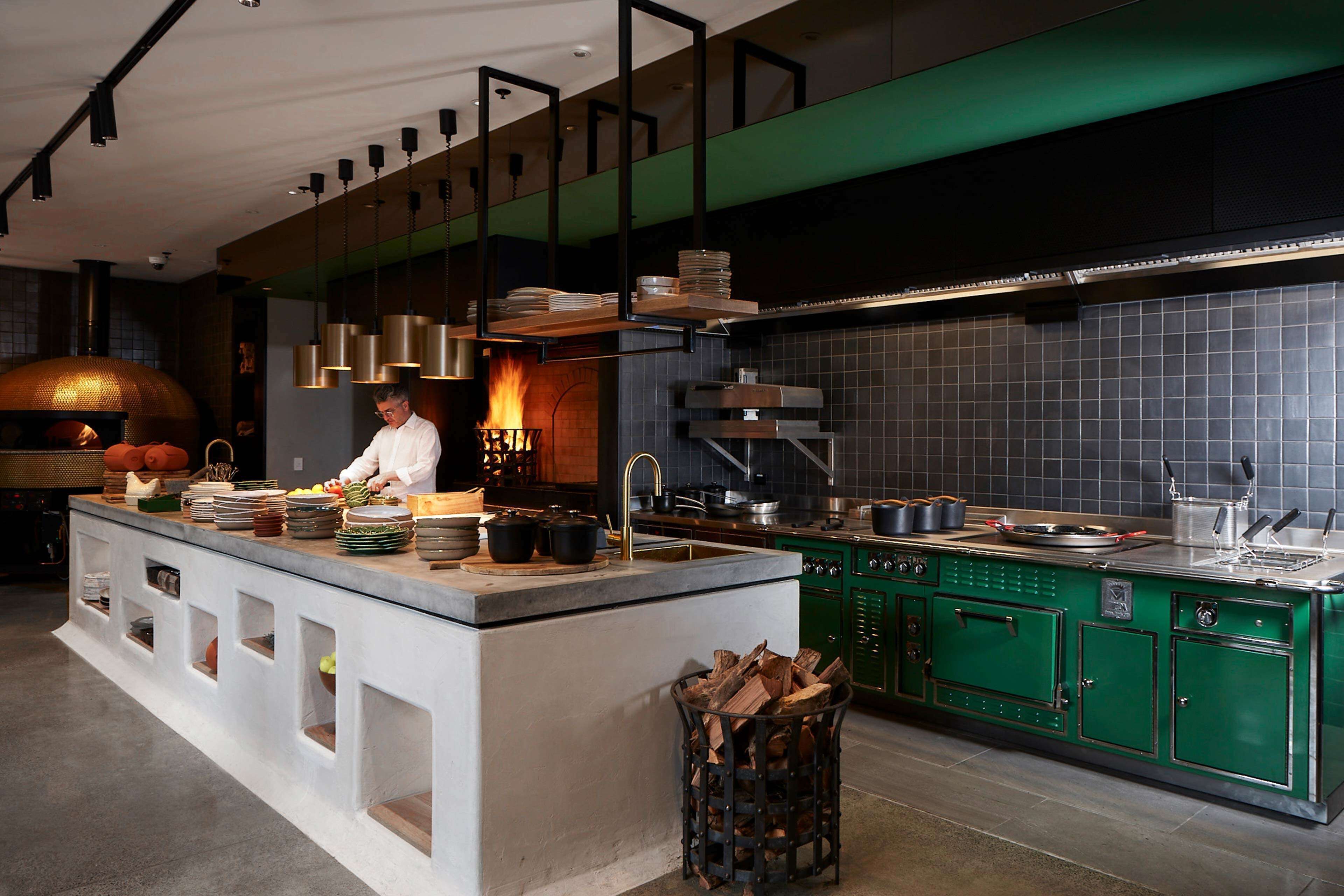 Una cocina moderna con un chef preparando comida, un horno grande y armarios verdes.