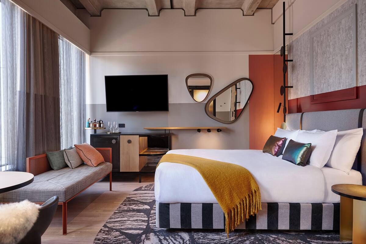 A modern hotel room with a large bed, a sofa, a desk, and a flat-screen TV.