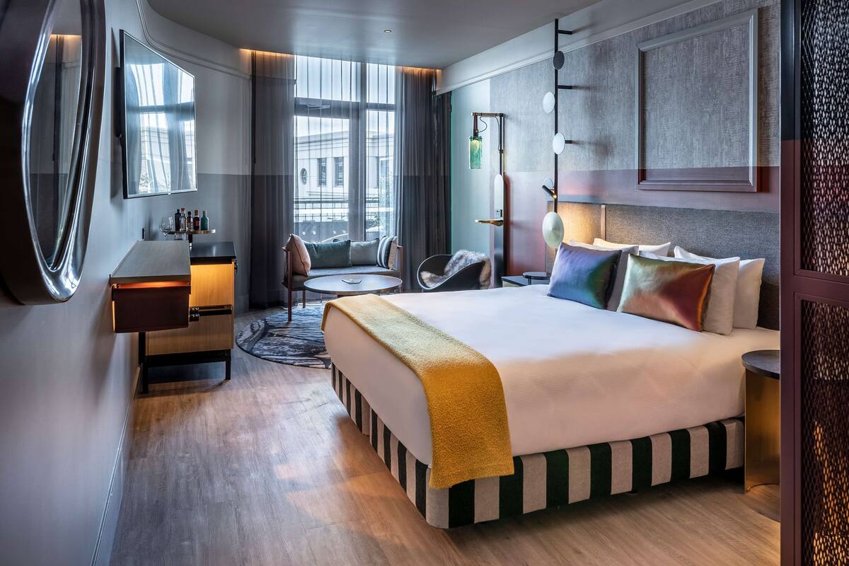 A modern hotel room with a large bed, a desk, a chair, and a round table.
