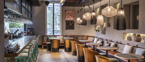 A modern bar area with wooden bar stools, hanging pendant lights, and a large window providing natural light.