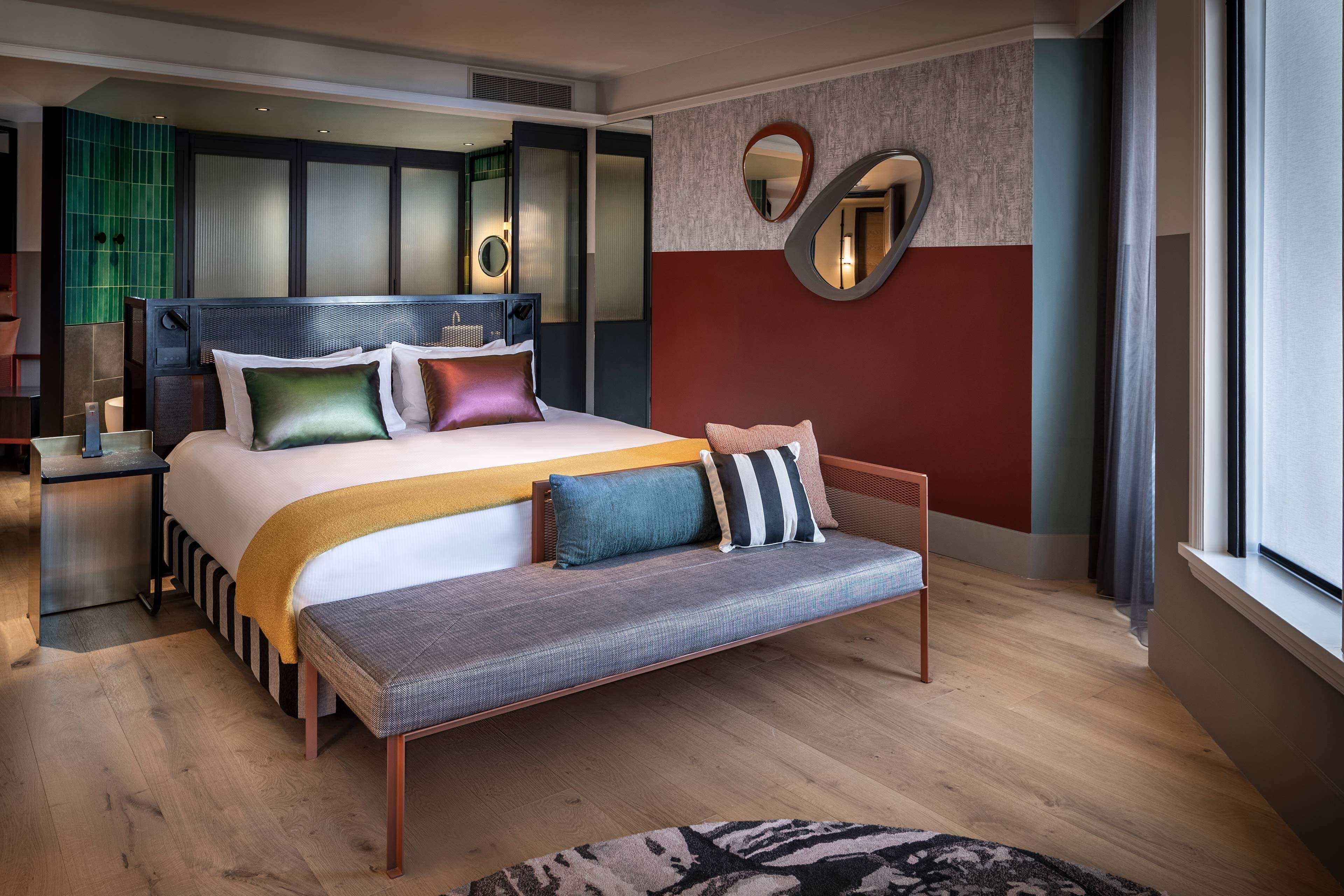 Une chambre d’hôtel moderne avec un grand lit, un banc et une vue sur la ville.