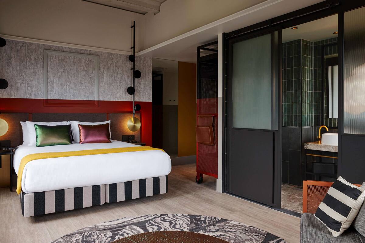 A modern hotel room with a large bed, a separate bathroom, and a sliding door leading to a balcony.