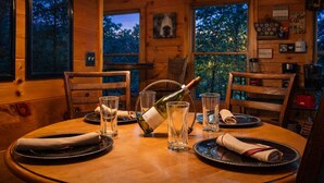 A wooden dining table set for four with wine glasses, a bottle of wine, and plates. - ♡♡ Cozy, Romantic Getaway w/Hot Tub & WiFi-Central Location (Sevierville)