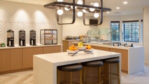 A modern kitchen with a central island, bar stools, a coffee station, and a view of the outdoors through large windows. - Staybridge Suites Carson City - Tahoe Area by IHG (Carson City)