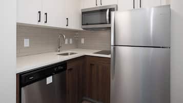 Una cocina con armarios blancos, un refrigerador de acero inoxidable, un lavavajillas y un microondas.