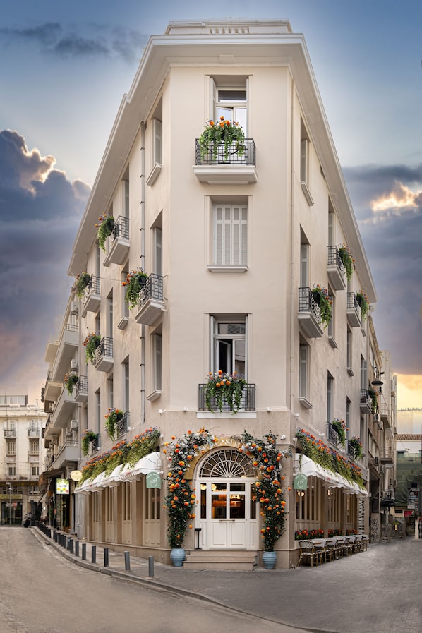 Un edificio de varios pisos con balcones, una entrada central con un arco decorativo y mesas al aire libre.