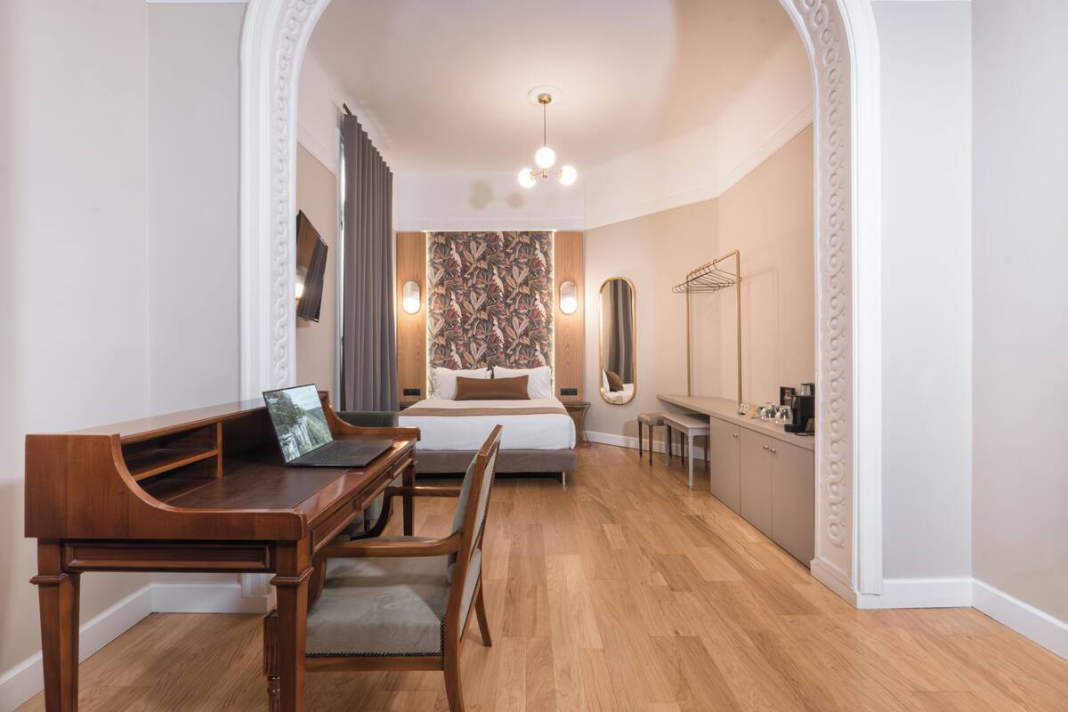 A bedroom with a wooden desk, a bed, a mirror, and a wardrobe.
