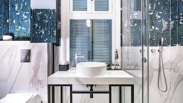 Un baño moderno con un lavabo blanco, paredes de mármol y una cabina de ducha de vidrio.