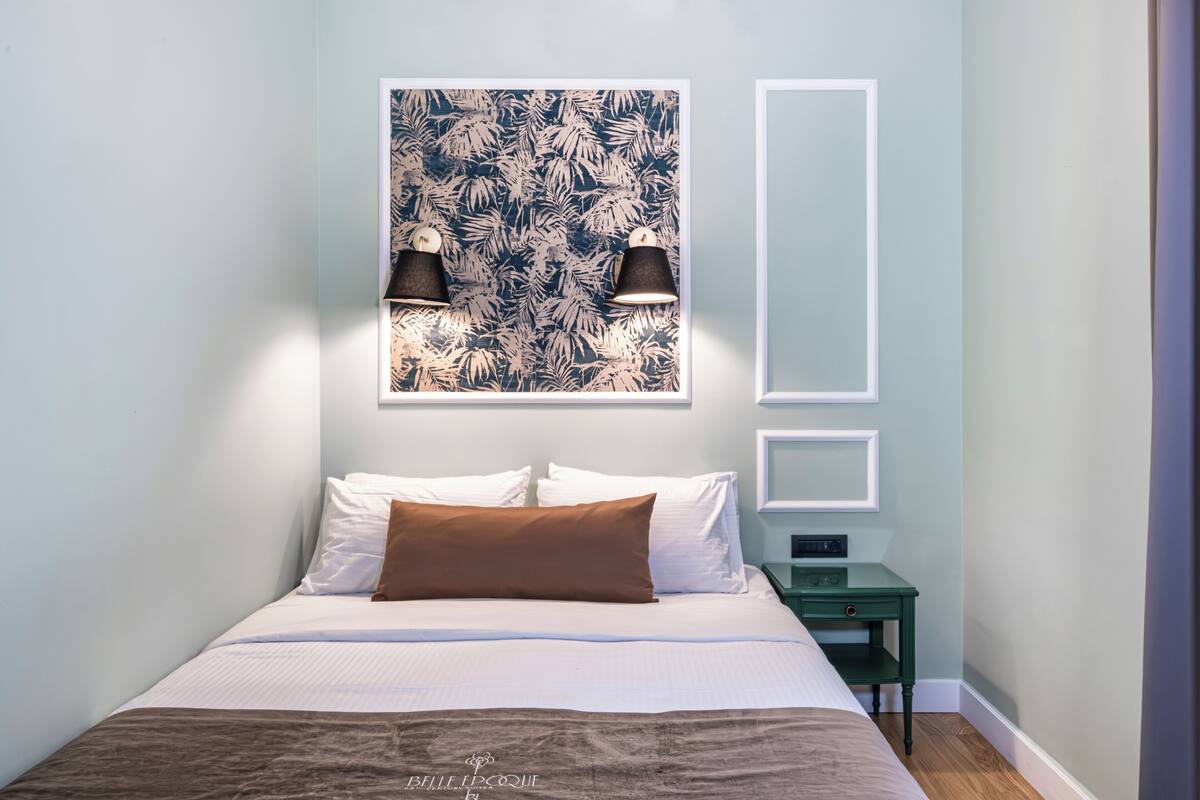 A neatly made bed with white and brown bedding, a wall-mounted light fixture, and a small green nightstand with a drawer.