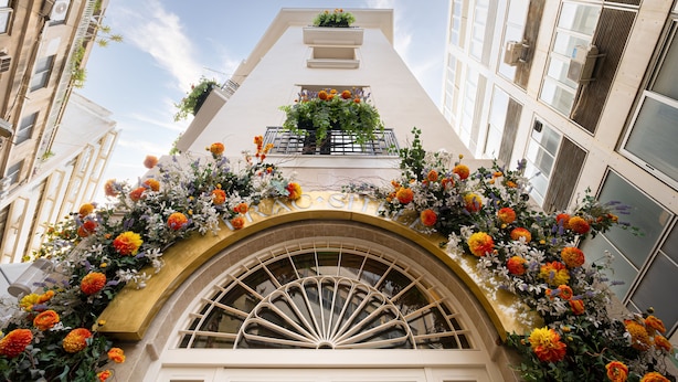 Fachada de edifício com uma grande janela em arco e varanda decorada com flores.