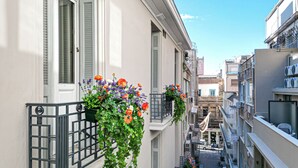 Uma rua estreita no centro da cidade, com edifícios de ambos os lados, varandas com caixas de flores e um céu azul claro.