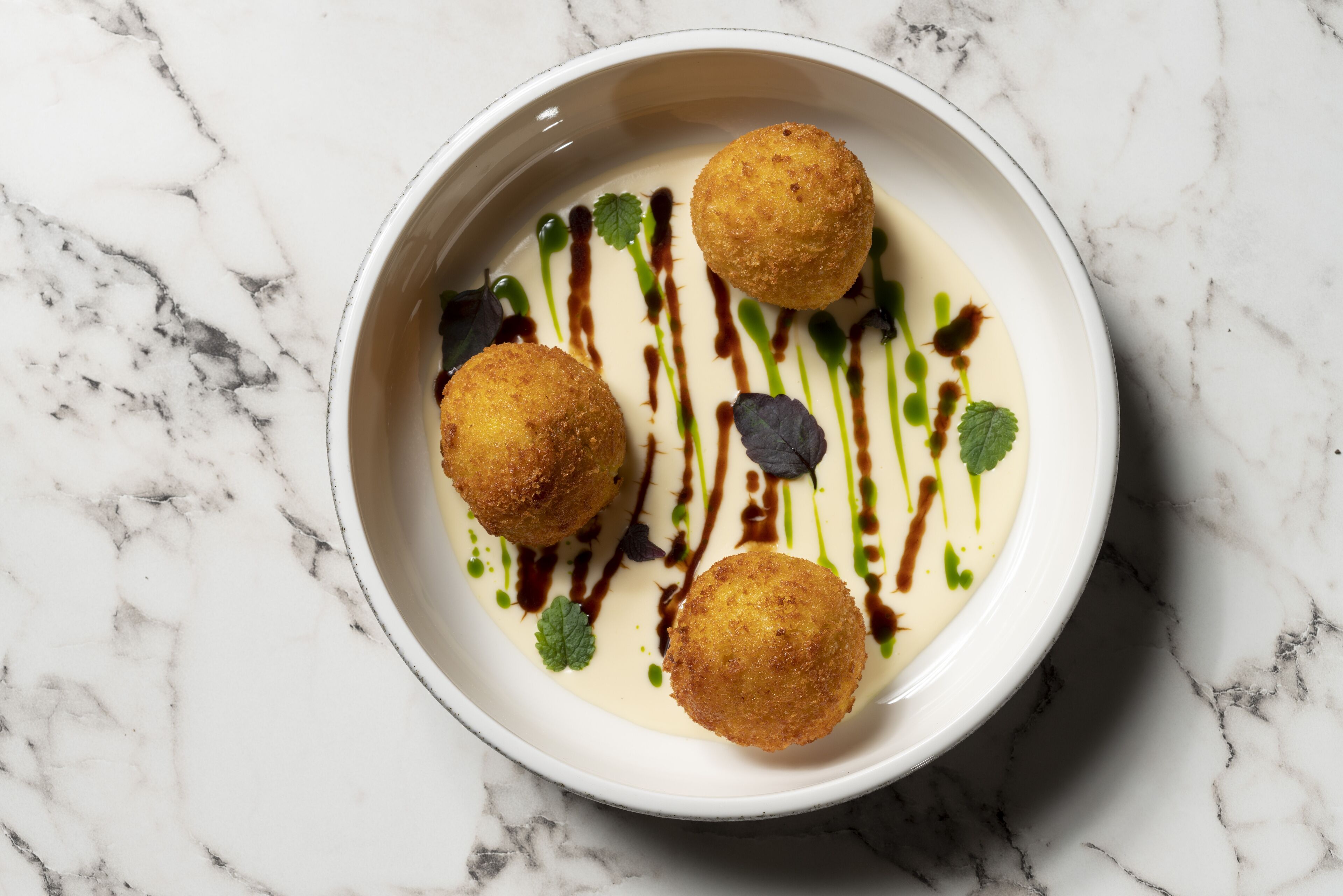 A white bowl with three golden-brown croquettes on a white marble surface.