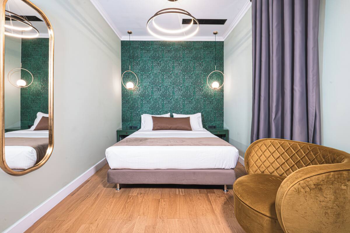 A modern hotel room with a large bed, a mirror, two bedside tables, a headboard, and a chair.